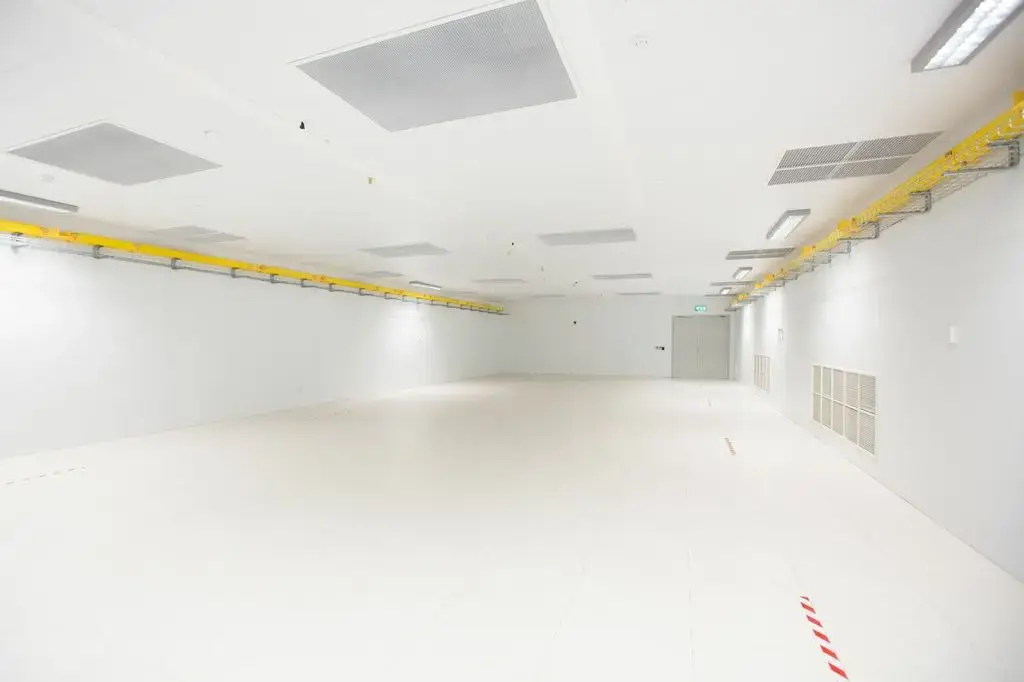 Empty white data hall with overhead yellow cable tray and floor markings, ready for fit-out.