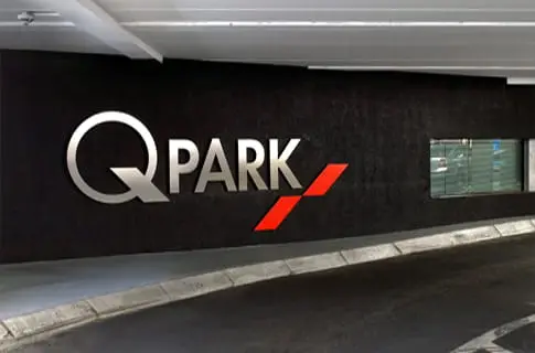 Illuminated Q-Park sign on a dark wall inside The Spire car park.