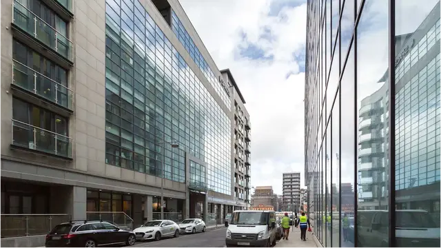 Street view of the building with contractors in high-visibility clothing at the entrance.