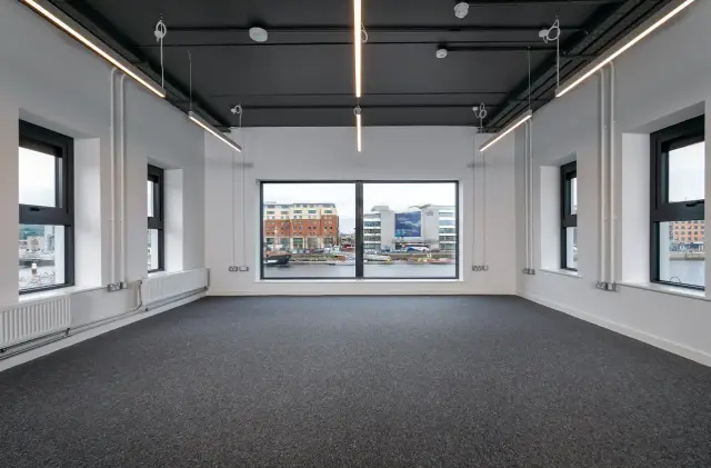 Open-plan office floor with suspended linear lighting and a window view across the Liffey.