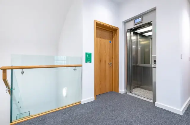 Lift lobby with glass balustrade, timber door and emergency exit signage.