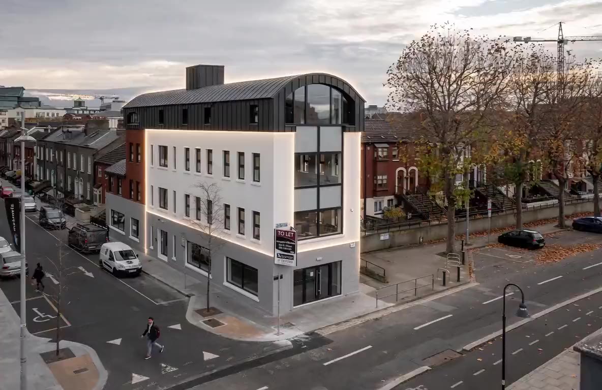 Corner office building at City Quay with a white rendered façade and a dark curved standing-seam roof.